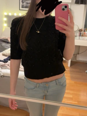 Svart croppad stickad topp - Säljer en svart croppad stickad topp med korta ärmar och små pärlor som detalj. Toppen har ett snyggt mönster i stickningen och ribbad kant nedtill. Den är i jätte bra skick och är nästan aldrig använd. Använd gärna köp nu