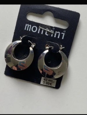 Öronhängen montini  - Bilderna visar ett par silvriga örhängen från Montini, ej silver. Har aldrig testats så fint skick fri frakt 