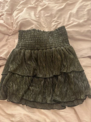 Glittrig Volangkjol  - Säljer min glittriga volangkjol från märket YEHWANG. Köpte använd på Sellpy 2022 och den har även använts av mig. Kort volangkjol med guld och silver glitter i tunt stretchigt material. Super cool både som kjol men även som en topp!🎀 Nypris 199 kr