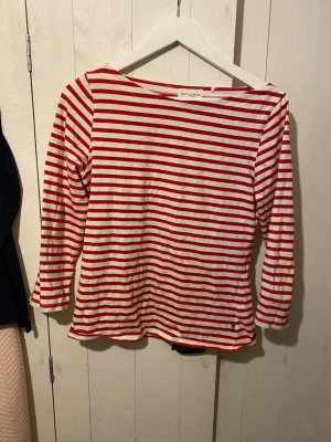 Randig långärmad topp Holly & Whyte - Säljer en vit och röd randig långärmad topp från Holly & Whyte by Lindex i storlek M. Toppen har en klassisk båtringad hals och är tillverkad i mjuk bomull. Perfekt för dig som gillar enkel och tidlös stil med lite färg.