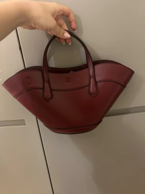 Vinröd handväska från H&M - Säljer min trendiga vinröda handväska från H&M. Superfin och fin färg. ALDRIG använd!!