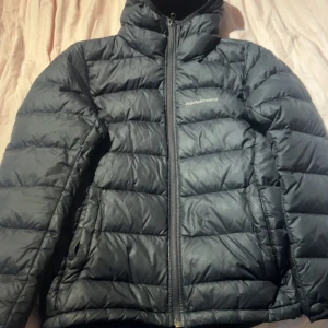 Svart dunjacka Peak Performance XS - Säljer en svart dunjacka från Peak Performance i storlek XS. Jackan är quiltad med horisontella sömmar, har hög krage och dragkedja framtill. Perfekt för kalla dagar och har en clean, sportig look.