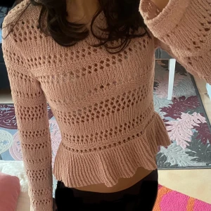 Rosa stickad tröja med volang - Säljer en söt rosa stickad tröja med volangdetalj i nederkant. Tröjan har ett genombrutet mönster och långa ärmar. Står xxs i storleken men passar mer som S. Perfekt för en mysig dag!