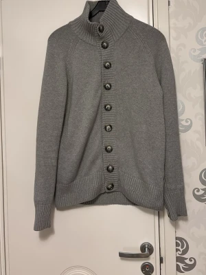 Grå cardigan från Matinique - Säljer en stilren grå cardigan från Matinique  med krage och stora knappar framtill. Tröjan är ribbstickad vid krage. Pris ej hugget i sten