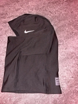 Svart ski mask  - Ski masken är tillverkad i ett syntetmaterial som andas och har en tight passform. Perfekt för träning och sportaktiviteter. Snygg detalj med Nike Pro-märke nedtill.