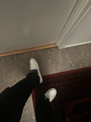 Valentino Garavani Rockstud sneakers - Säljer ett par vita Valentino Garavani Rockstud sneakers med coola nitar runt hälen och en svart detalj över snörningen. Skorna är i skinn och har rund tå samt platt sula. Perfekt för dig som vill sticka ut med lyxig streetstyle.