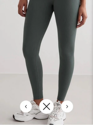 Mörkgröna ribbade leggings - Snygga mörkgröna leggings med ribbad struktur och tight passform. De har hög midja och är tillverkade i ett mjukt och stretchigt syntetmaterial som sitter skönt mot kroppen. Perfekta för träning eller chill dagar. Färgen är diskret och passar till det mesta. De är inte använda jättemycket men har ett litet märke på knät som knappt syns, kan skicka bild vid intresse. Köpta för 699kr