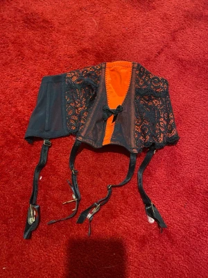 Svart och röd strumpebandhållare - Säljer garter bely från Lella M i storlek XS. svart med röda detaljer, spets samt en liten rosett framtill. Justerbara remmar / strumpeband med metallspännen och fästen. 