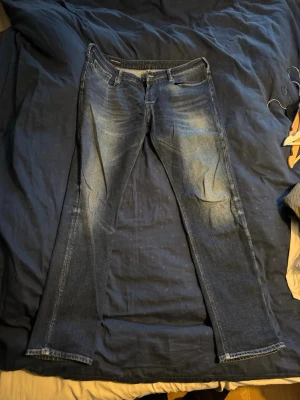 Emporio Armani blå jeans straight fit - Snygga blå jeans från Emporio Armani med klassisk femficksdesign och ikonisk logga på bakfickan. Jeansen har raka ben och subtila slitningar framtill för en cool look. Tillverkade i mjukt bomullsjeansmaterial med normal passform.