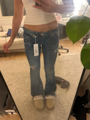 Blå low rise flare jeans  - Säljer ett par blå low rise flare jeans från gina tricot i storlek S. Jeansen har slitna detaljer vid knäna och fickorna, kontrastsömmar och snygg broderad bakficka. Materialet är klassisk jeans med stretch och passformen är bootcut med låg midja.