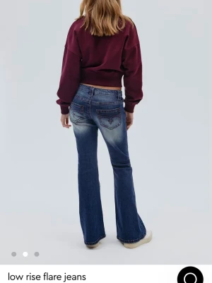 Blå low rise bootcut jeans - Snygga blå jeans med låg midja och bootcut-ben. Jeansen har klassisk femficksdesign, röda dekorativa sömmar och lätt slitna detaljer. Materialet är jeans med en mjuk känsla och stretch. Perfekt för dig som gillar retrovibbar och vill ha en cool siluett. Ganska lika de trendliga kvarg jeansen på framsidan! Pris går att diskutera!!