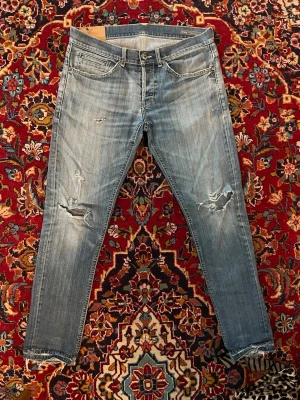 Ljusblå George jeans från Dondup - Tja! Säljer ett par ljusblå George jeans från Dondup med slitna detaljer och trasiga knän. Jeansen är i bra skick men använda.  De har snygga råa kanter vid bensluten. Tillverkade i Italien med bomull med lite stretch för extra komfort.