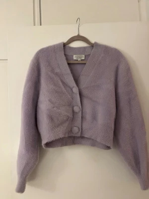 Ljuslila fluffig kofta från & Other Stories - Supermjuk och fluffig ljuslila kofta från & Other Stories. Koftan är croppad med stora klädda knappar framtill och har lång ärm. Perfekt för lager-på-lager och ger en mysig vibe till din outfit.