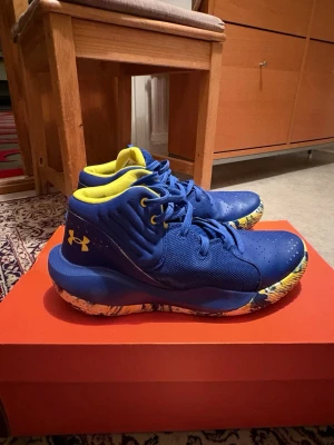 Blå sneakers från Under Armour - Säljer ett par blå sneakers från Under Armour med gula detaljer och logga. 