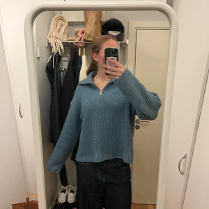 Blå stickad tröja med half zip - Mysig blå stickad tröja med halv dragkedja och krage. Tröjan har en loose passform och långa ärmar, perfekt för kyligare dagar. Enkel att styla med jeans eller kjol för en avslappnad look.