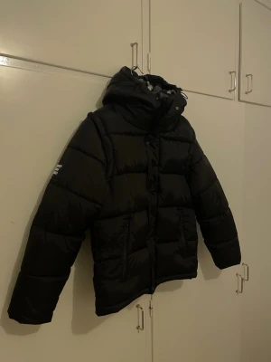 Svart pufferjacka från Burberry M - Säljer en svart pufferjacka från Burberry i storlek M. Jackan har huva, och dragkedja kan bli till en väst helt ny aldrig använd säljer den pågrund av att den är liten 