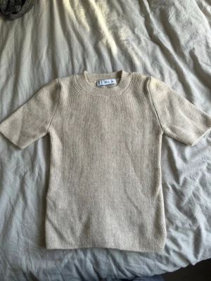 Beige stickad kortärmad tröja från mango  - Säljer en beige stickad tröja från Mango med ribbad struktur. Tröjan har korta ärmar och rund halsringning, perfekt för lager på lager under höst och vår. Enkel och stilren design som passar till det mesta.