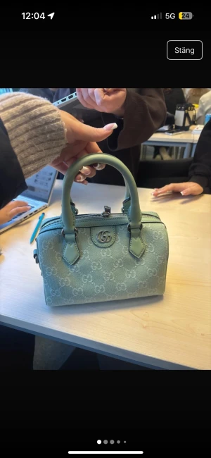 Mintgrön handväska från Gucci - Superfin mintgrön handväska från Gucci med klassiskt GG-mönster över hela väskan. Väskan har två stadiga handtag, silverfärgad dragkedja och detaljer i skinn. Perfekt storlek för det viktigaste och riktigt snygg att bära till alla outfits. Använd 1 gång och köpt i Italien i en Gucci butik. Har kvitto, dustbag och påse lådan är däremot slängd! Pris kan diskuteras och möts upp i Stockholm🩷🫰🏼
