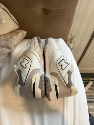 Helt nya New Balance 550 sneakers - Säljer ett par stilrena New Balance sneakers i vitt och ljusgrått med klassisk N-logga på sidan. Skorna har snörning, perforerade detaljer och en chunky sula för extra komfort. Perfekta för dig som gillar en clean och sportig look.