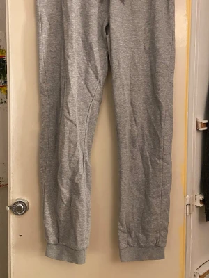 Grå mjukisbyxor från Champion - Grå mjukisbyxor från Champion med broderad logga på höften. Byxorna har resår i midjan och vid bensluten för en skön passform. Tillverkade i mjukt bomullsmaterial, perfekta för chill eller träning.