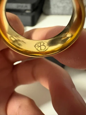 Bred guldfärgad ring från By Billgren - Säljer en bred och stilren guldfärgad ring från By Billgren. Ringen har en slät och blank yta som ger en snygg och modern look. Perfekt accessoar för att lyfta din outfit. Passar både killar och tjejer som gillar statement-smycken. Det är en medium 20 mm storlek ring.