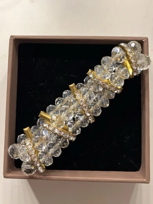 Glittrig armband med pärlor och guld - Säljer ett glittrigt armband med stora, transparenta pärlor och guldfärgade detaljer. Armbandet har flera rader av gnistrande stenar och guldfärgade, en sten har dock fallit av💕