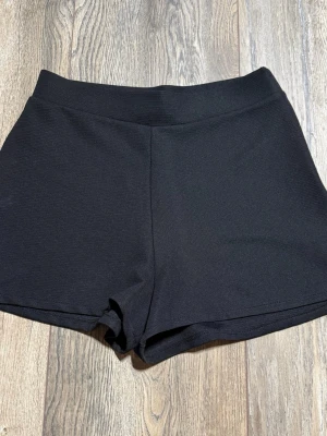 Svarta shorts från Zara med dragkedja - Säljer ett par svarta, högmidjade shorts från Zara i storlek S. De har en clean look med diskret struktur i tyget och en smidig dragkedja i sidan. Perfekta till sommaren och lätta att matcha med olika stilar.