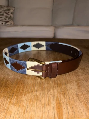 Mörkblå-vit bälte - Helt nytt och inplastat mörk blått och vitt färgat broderat bälte i färgerna: mörkblå och ljusblå och vit. Extremt fräscht bälte som ger din outfit en sista detalj. Finns 5 olika storlekar att välja mellan: 80-110 cm. Hör av er vid minsta fundering!