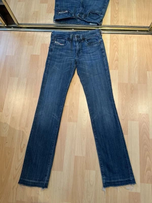 Blå Diesel jeans bootcut - Lågmidjade Diesel-jeans i mörkblå tvätt. Snygga fickor med diskreta diamantdetaljer. Jeansen är köpta via UF men har tyvärr aldrig kommit till användning då de var för små. Jeansen är i mycket fint skick. Lätt fransad nederkant.