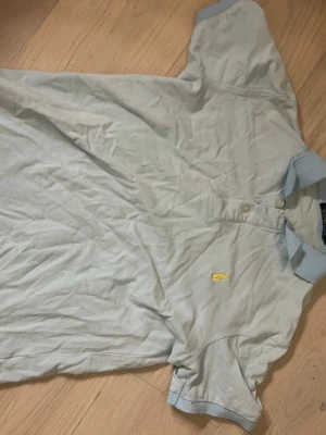 Ljusblå Ralph Lauren piké - Säljer en ljusblå pikétröja från Ralph Lauren med klassisk krage och knappar framtill. Tröjan har gul broderad logga på bröstet och RLX-detalj på ärmen. Tillverkad i mjuk bomull och har korta ärmar.