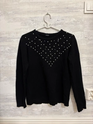 Svart stickad tröja med pärlor OOTD - Snygg svart sopastickad tröja från OOTD med pärldetaljer i ett V-mönster över bröstet. Tröjan har rund halsringning och långa ärmar, perfekt för dig som vill ha något både stilrent och lite extra.