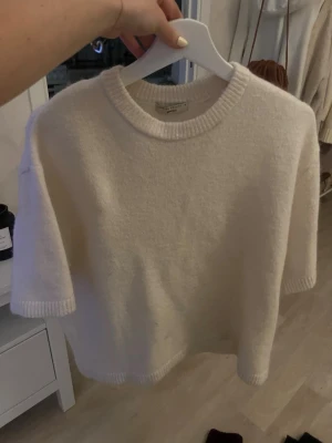 Vit stickad kortärmad tröja - Mysig vit stickad tröja från Gina med korta ärmar och rund hals. Tröjan har ribbade detaljer vid hals, ärmslut och nederkant. Perfekt för lager på lager under kyligare dagar.