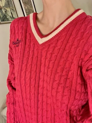 Röd kabelstickad tröja från Sebago - Riktigt snygg vintage röd kabelstickad tröja från Sebago med vit v-ringad kant och broderad logga på bröstet. Långa ärmar med vit detalj vid mudden. 
