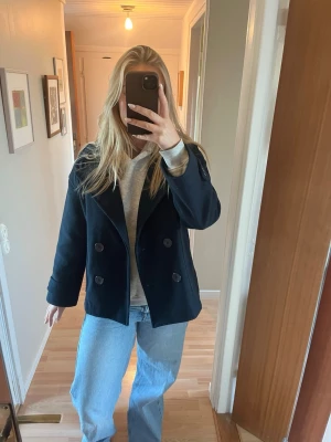 Mörkblå skepparkavaj med knappar - Säljer en mörkblå skepparkavaj med dubbelknäppning och bred krage. Jackan har två stora fickor framtill och är helfodrad. Klassisk och stilren modell som är enkel att matcha med jeans eller hoodie. Perfekt för dig som gillar en chill och tidlös look.