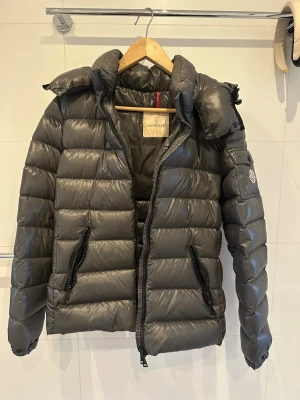 Mörkgrå Moncler dunjacka - Säljer en mörkgrå Moncler dunjacka med hög krage och två dragkedjeförsedda fickor. Jackan har Moncler-logga på ärmen och quiltad design. Modellen heter ”bady” och är i storlek 3. Kvittobevis finns och den köpte på NK i Göteborg. Inga defekter eller ngt sådant.