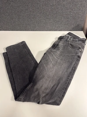Grå Lee jeans straight fit - Säljer ett par grå jeans från Lee med klassisk femficksdesign och raka ben. Jeansen har normal passform och är tillverkade i mjukt denimtyg. Snyggt slitna detaljer och Lee-logga på bakfickan samt läderpatch i midjan. Skriv angående frågor!