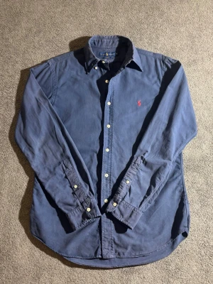 Blå skjorta från Ralph Lauren Slim Fit - Klassisk blå skjorta från Ralph Lauren i slim fit-modell. Skjortan har broderad logga på bröstet och är i väldigt fint skick🤩 skjortan har inga skador eller fläckar nypris:1200kr mitt pris:449kr det är bara att höra av dig om du har några funderingar och priset är aldrig hugget i sten 🪨✅