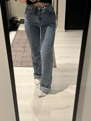 Blå jeans high waist - Blåa jeans med hög midja. Passformen är loose med raka ben. Jeansen har knappgylf med 5 knappar. 