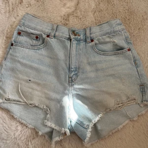 Ljusblå jeansshorts från Zara - Säljer ett par ljusblå jeansshorts från Zara med fransiga kanter och slitna detaljer. Modellen är midwaist med små revor på framsidan. Perfekt för dig som gillar en chill och trendig look på sommaren.☀️💘☺️