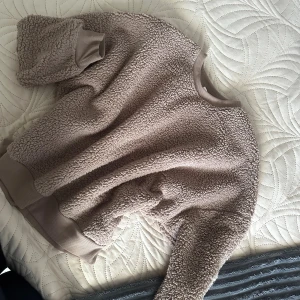 Beige teddytröja med ribbade muddar - Supermjuk och mysig beige teddytröja med ribbade muddar vid ärmslut, hals och nederkant. Perfekt för kyliga dagar och har en loose fit som ger en avslappnad vibe. Passar dig som gillar en enkel men trendig look.