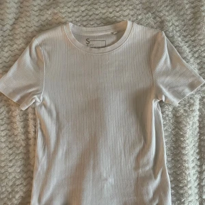 Vit ribbad t-shirt från New Yorker - Snygg vit ribbad t-shirt från New Yorker i storlek S. T-shirten har korta ärmar, rund halsringning och är tillverkad i ett mjukt, stretchigt material som sitter skönt på kroppen. Perfekt till jeans eller kjol för en clean och fräsch look.Har använt den typ 3 gånger💕