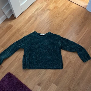 Mörkgrön stickad tröja från KappAhl - Mysig mörkgrön stickad tröja från KappAhl i storlek 164. Tröjan har en klassisk rund halsringning och är ribbstickad vid ärmslut och nederkant. Perfekt för kyliga dagar och enkel att matcha med jeans eller kjol.