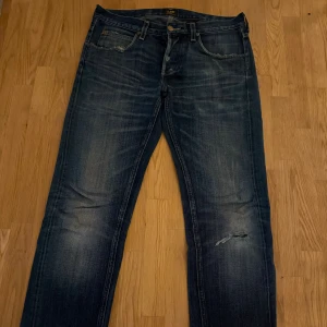 Blå jeans från Lee ”101S” med slitning - Snygga blå jeans från Lee ”101S” med klassisk femficksdesign och slitningar på knäet för en cool, avslappnad look. Jeansen har raka ben och tydliga tvättade detaljer som ger en vintagekänsla. Perfekta för dig som gillar en streetig stil.