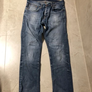 Blås nudie jeans  - Säljer ett par blå skinny jeans från Nudie med slitningar och lagade detaljer på benen. Jeansen har klassisk femficksdesign, normal midja och är tillverkade i stretchig denim för en tajt passform. Snyggt tvättade med ljusare partier och Nudie-logga på bakfickorna.