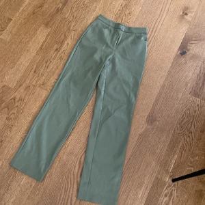 Olivgröna kostymbyxor i skinn från NA-KD - Snygga olivgröna kostymbyxor från NA-KD i fejkskinn. Byxorna har medelhög midja, raka ben och diskreta fickor både fram och bak. 