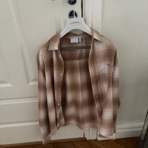 Beige gul rutig skjorta  - Säljer en snygg beige och vit rutig skjorta. Skjortan har klassisk krage, bröstficka och knäppning framtill. Långärmad modell i mjukt material som sitter skönt och passar perfekt till jeans eller chinos.