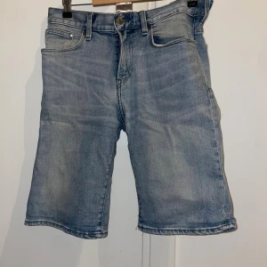 Ljusblå jeansshorts med fickor - Snygga ljusblå jeansshorts med klassisk femficksdesign och knappgylf. Modellen har raka ben och normal passform, perfekt för chill dagar. Materialet är slitstarkt denim och shortsen har bälteshällor och detaljerade sömmar. Enkelt att matcha med t-shirt eller hoodie.
