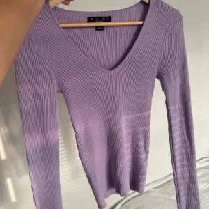 Ljuslila ribbad tröja från Amisu - Supersnygg ljuslila ribbad tröja från Amisu med v-ringning och lång ärm. Perfekt för dig som vill ha en enkel men trendig look. Mjuk och stretchig, passar till allt!