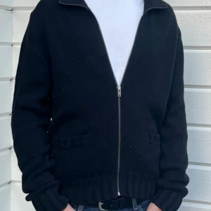 Svart kofta från Polo Jeans Co Ralph Lauren - Svart stickad kofta från Polo Jeans Co Ralph Lauren i 100% bomull. Modellen har hel dragkedja framtill, ribbade muddar och två fickor. Perfekt för lager-på-lager och enkel att matcha med jeans eller t-shirt. Passar M och L