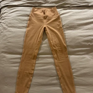 Rosa/ bruna lululemon leggings - Snygga rosa/bruna leggings med hög midja och tight passform. De är stretchiga och sitter skönt mot kroppen, perfekta för en chill look eller till träning. Materialet känns mjukt och följsamt. Har kortet som man får vid köp av leggingsen. 